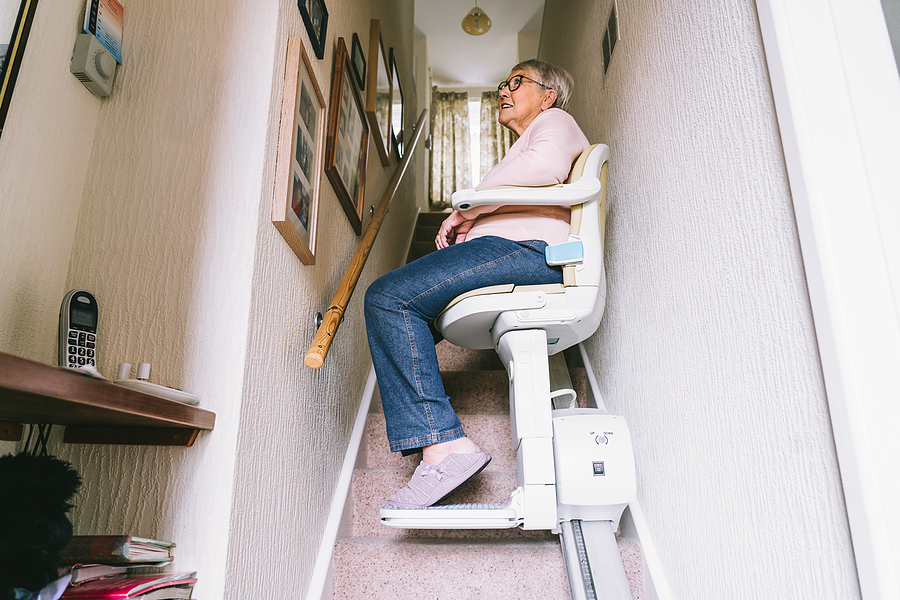 Senior Woman Using Automatic Stair Lift On A Staircase At Her Ho
